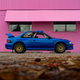 side profile photo of a blue subaru 2.5rs parked in front of a bright pink building